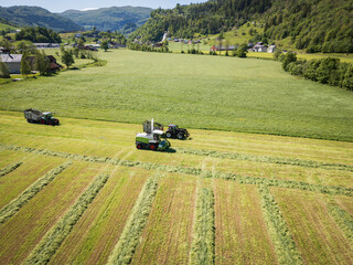 Drone view of the fodder harvesting process in Norway: agricultural machinery collects mown grass...