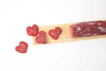 Heart-shaped slices of cured sausage on a wooden board with a whole sausage. Minimalistic food presentation. Valentine Day food concept. Flat lay composition with copy space.