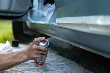 Close-up of a man's hand pressing a spray can during car painting. Detail of auto repair work with...