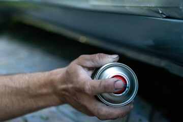 Dirty hand pressing spray can nozzle while repainting a car. Strong detail of real-life garage repair process