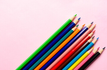 A collection of colorful pencils on a pink background.