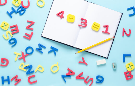 Math equation with numbers and symbols on notebook with colorful alphabet letters scattered on light blue background. Back to school concept. - Powered by Adobe