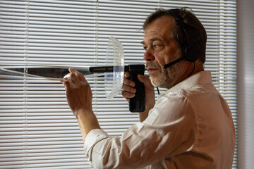 A male spy with a listening device at a window. A man wearing headphones watches closely through...