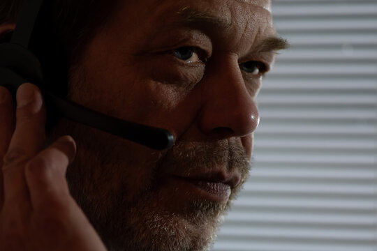 Close-up of a surveillance scene. Close-up of a man's face with a headset watching the action behind the blinds.