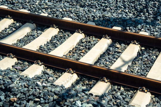 This image, reflecting a transportation concept, shows a close-up of modern railroad tracks with concrete sleepers embedded in dark ballast.