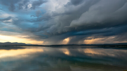 Obraz premium Dramatic sunset storm clouds over calm lake and mountains