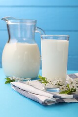 Fresh milk and blossoms on light blue table, closeup
