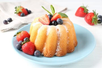 Tasty Bundt cake with powdered sugar and berries on white wooden table, closeup