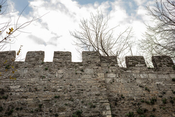 Medieval stone fortress wall with battlements under cloudy sky