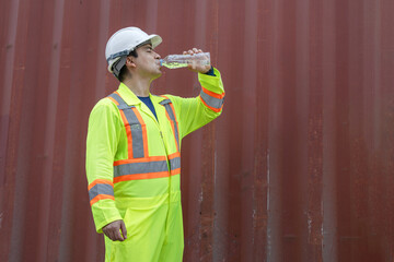 Worker man in hard hat drinking water at containers cargo, Construction site worker drinking water,...