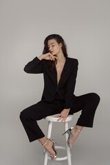 Confident Woman In Black Suit Sitting Elegantly On A Stool 