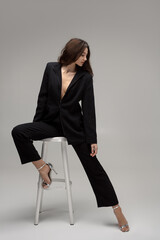 Confident Woman In Black Suit Posing Elegantly On A Stool 