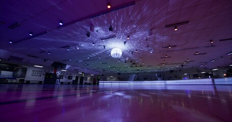 Disco ball shining over empty roller skating floor with colorful lights - wide, low shot - Powered by Adobe