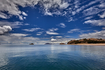 A scenic view of Lake Titicaca’s northern side from the Capachica Peninsula, showing Andean hills, deep blue waters, and traditional farmland under dramatic stormy skies.