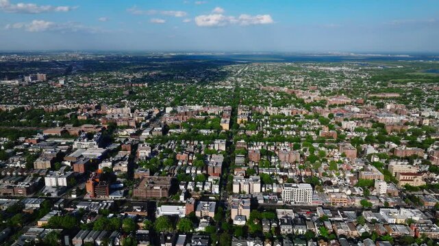 Aerial view of a residential neighborhood in Brooklyn, New York City, captured on a clear spring day. The image features mid-rise apartment buildings, tree-lined blocks, and dense housing patterns ext
