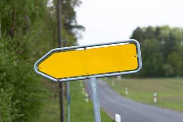 Empty yellow traffic sign in an arrow shape pointing to the left. Guidance with a location name in Germany. Travel destination in a rural area mockup. Template of a signage at a country road.