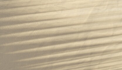 Soft window blind shadow casting horizontal light stripes on beige fabric background