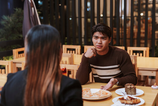 A frustrated young man expresses displeasure during a restaurant date with an older woman, showing concern or being finicky about the subpar food or conversation.
