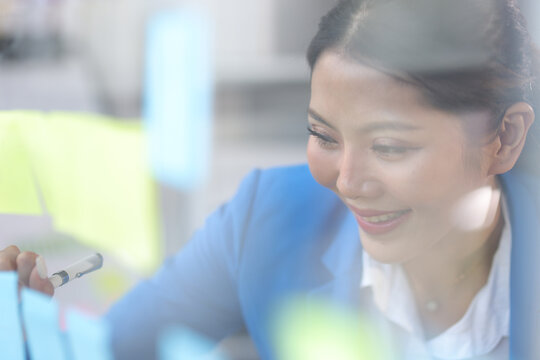 Thoughtful businesswoman thinks creatively and sketches initial business planning with paper stickers on a transparent board. Strategy analysis and business planning.