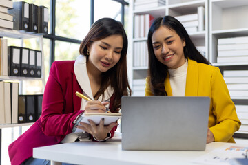 Asian businesswoman and colleague discussing new project on laptop in office.