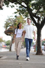 Fototapeta premium Two young tourists happily walk hand in hand in a tourist area in a city in Thailand.