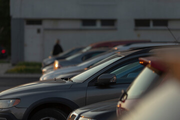 A large parking lot is filled with a variety of silver cars, while a person can be seen walking in the background
