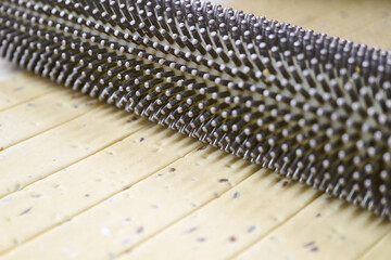 Cracker dough being perforated by a docking roller before baking for consistent texture and flavor enhancement