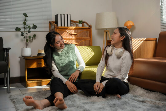 Two happy female friends spending leisure time together at home, enjoying conversation and laughter in a cozy living room setting