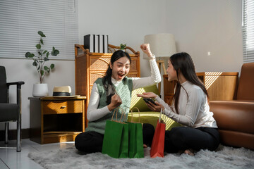 Two asian women are celebrating a successful online purchase using a smartphone, showing excitement...