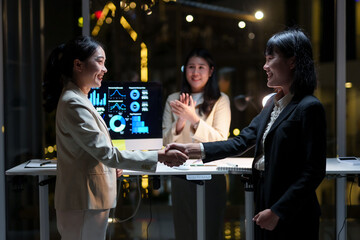 Asian businesswomen shaking hands after successful presentation, celebrating business deal in modern office at night