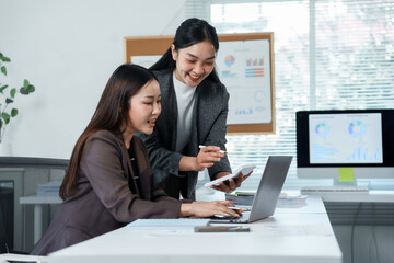 Two asian businesswomen are discussing and working together using laptop and calculator in the office