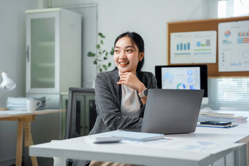 Fototapeta premium Happy entrepreneur woman sitting at desk and working using laptop computer in modern office, looking away and smiling
