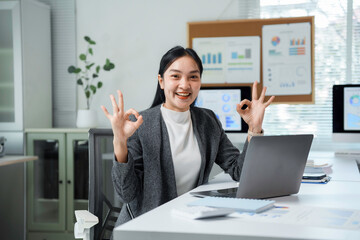 Naklejka premium Happy manager smiling and making an ok sign while sitting at a desk in a modern office, exuding confidence and professionalism