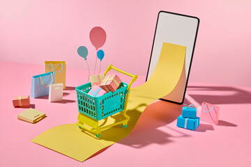 Colorful paper shopping elements with balloons float around a basket and smart phone, celebrating...
