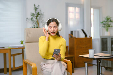 Relaxed Asian businesswoman enjoying music during a break in her modern home office, smiling happily while sitting comfortably in a chair