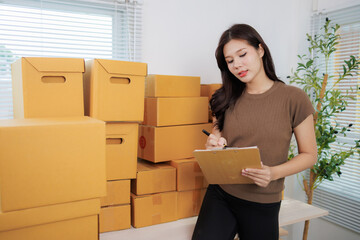 Young asian woman entrepreneur checking order on clipboard while working in a warehouse full of...