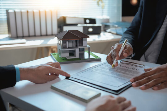 Real estate agent pointing at contract details while showing new house scale model to client in office