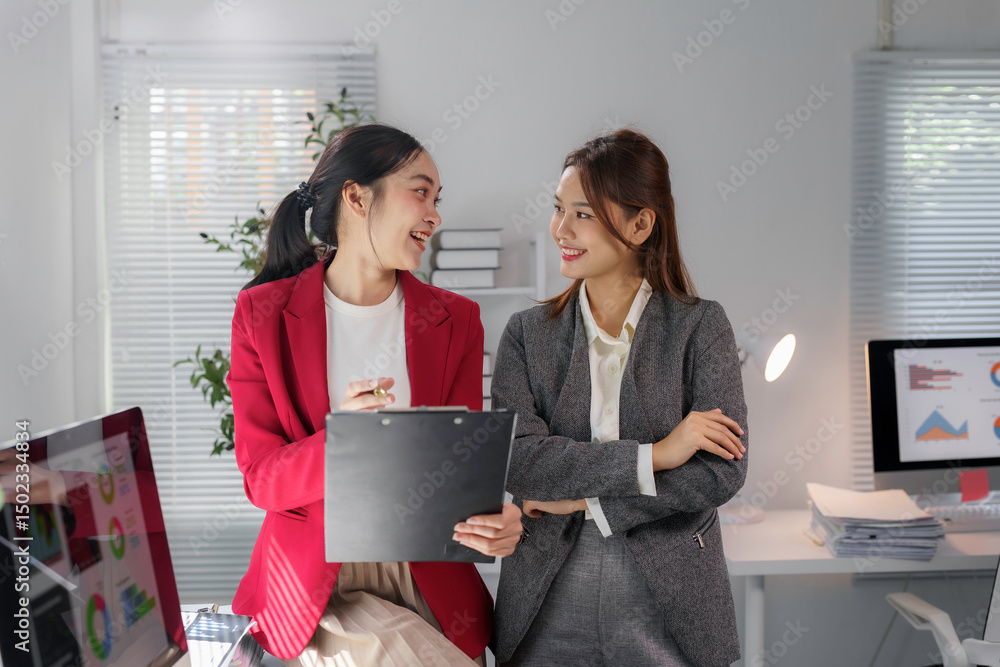 Poster two asian businesswomen are discussing and analyzing data using a clipboard and computer in a modern