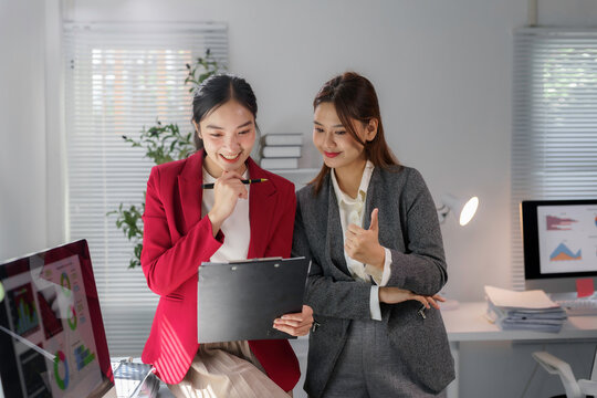 Two Asian businesswomen reviewing statistics on a clipboard, discussing positive results and collaborating on strategies for success
