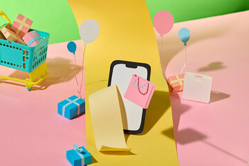 A playful paper arrangement shows a smart phone "scrolling" a shopping receipt near a shopping basket. Colorful paper cutting props, convenient online shopping illustration at home