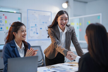 Asian businesswomen engaging in a handshake after successfully closing a deal during a meeting in a modern office setting
