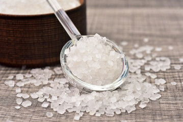 Crystal sugar in glass spoon with woonden bowl background. Sugar type are fructose, glucose, lactose. Over consumption can be weight gain, type 2 iabetes and heart disese.