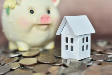 White house on the coins with piggy bank background. Saving for a house typically involves accumulating funds for a down payment, pay deposit; Mortgage Loan, Housing loan; installments.