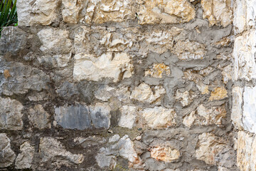 Fototapeta premium In the foreground is a fragment of a stone wall made of grey stone of various textures and sizes.