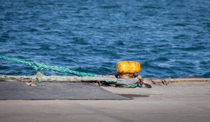 Concrete pier. Old, rusty yellow bollard and attached ropes.