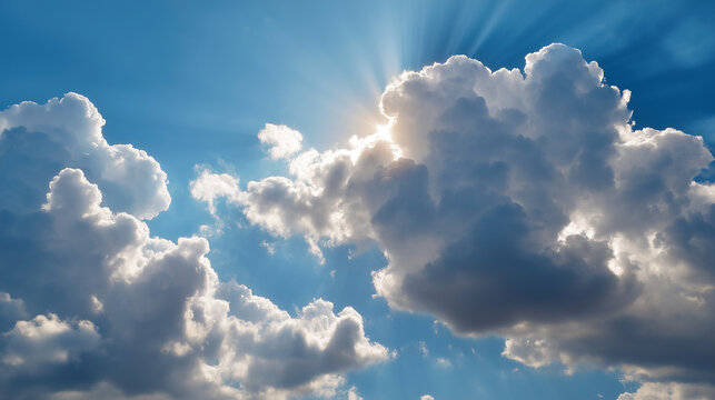 A scenic view of a bright blue sky filled with large, soft clouds. The sun is partially hidden behind the clouds, casting warm light rays.