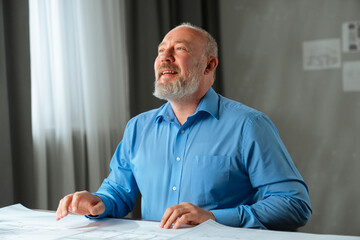 An architect sits in an office at a desk with blueprints