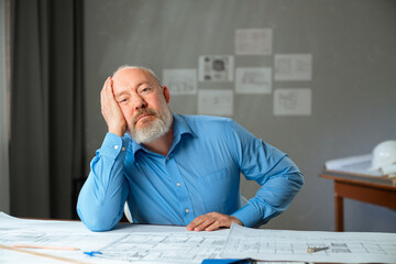 An architect sits in an office at a desk with blueprints