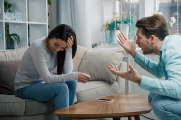 Couple arguing at home, woman covering face while man gestures emotionally