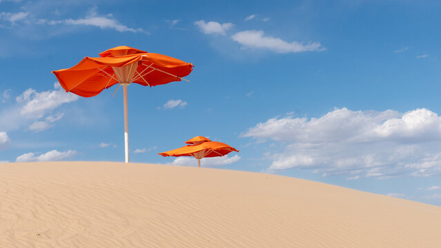 Orange umbrellas on a sandy desert under a blue sky - Powered by Adobe